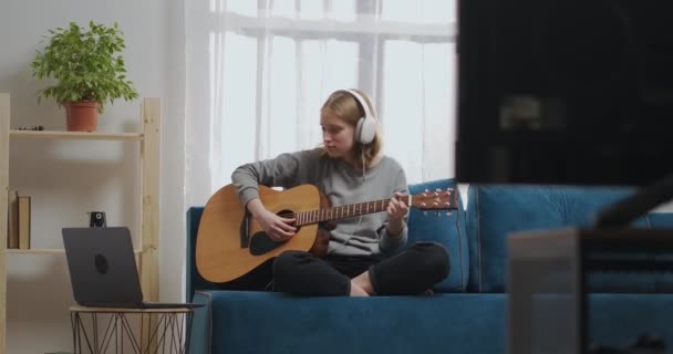 Adolescente ragazza sta usando guida di auto-aiuto per suonare la chitarra sul computer portatile, strappare le corde, seduto da solo a casa durante il fine settimana — Video Stock