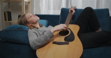 Sarı saçlı genç bir kız beyaz bir oturma odasındaki yumuşak bir kanepede uzanıyor ve kafasını kaldırıyor. Bir kadın müzik enstrümanında rahatlatıcı bir melodi çalar.
