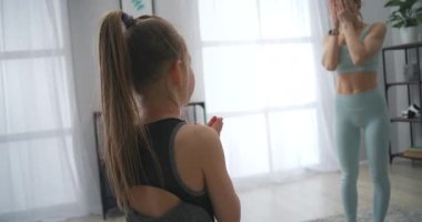 Kadın ve kız çocuk oturma odasında blöf yapıyor, anne ve kız spor kıyafetleri giyiyor.