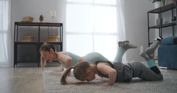 Niña en edad preescolar está entrenando en casa, la madre está aprendiendo hija a hacer flexiones, inculcar buenos hábitos — Vídeos de Stock
