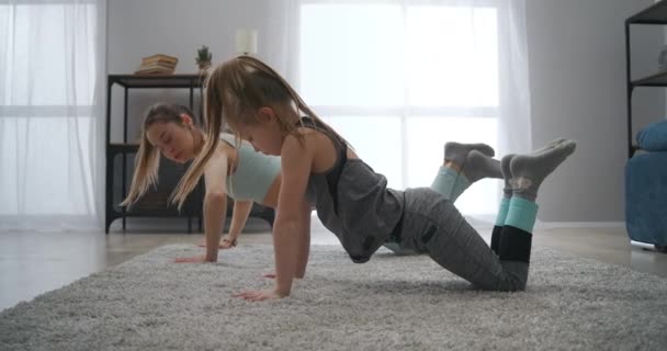 Fetița și mama ei fac flotări în camera de zi, stil de viață sănătos și exerciții fizice, fitness acasă — Videoclip de stoc