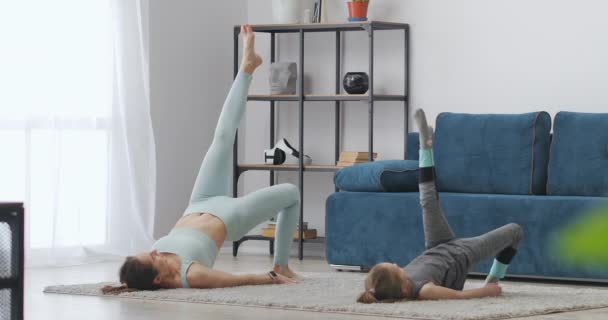 Pagi latihan dari gadis kecil dan ibunya di ruang tamu, ibu dan anak berbaring di lantai — Stok Video