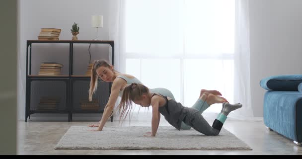 Mujer deportiva está entrenando a su hijo para hacer flexiones, madre e hija están entrenando juntos en el apartamento — Vídeos de Stock