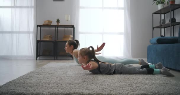 Trening gimnastyczny młodej matki i córeczki, leżących na podłodze w pokoju i rosnących tułowia, sportowej rodziny — Wideo stockowe