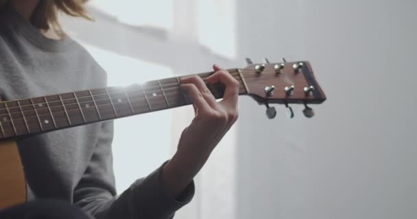 10代の若者が美しい日差しと白いリビングルームでギターを演奏します。女性は屋内で音楽を作曲する。そのアーティストはアコースティックギターを演奏する。女の子は楽器を練習している。動作中の撮影 — ストック動画