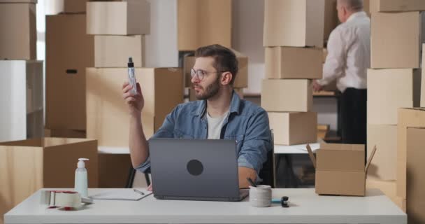 Small business owner generates an order for delivery to buyers. Businessman puts two bottles of household chemicals in a cardboard box. Man writes with a ballpoint pen on a paper document. — Stock Video