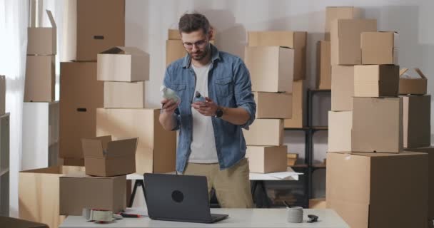 Los hombres de negocios revisan las mercancías antes de la entrega a los clientes. El hombre pone los productos químicos domésticos uno por uno en una caja de cartón. — Vídeos de Stock