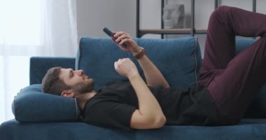 Rahat adam internette sörf yapıyor ve haber kasetlerini akıllı telefondan izliyor, evdeki kanepede yatıyor.