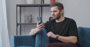 Genç adam kazanarak seviniyor, akıllı telefondan mesaj okuyor evde oturuyor, çılgın bir sevinç içinde.