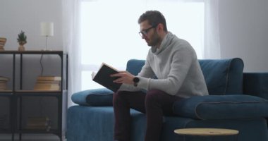 Yakışıklı adam hafta sonunu evde kitap okuyarak, sakin ve rahat bir ortamda oturma odasında geçiriyor.