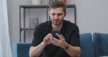 Düşünceli adam evdeki akıllı telefonuyla kumar oynuyor ve kazanıyor, duygusal olarak seviniyor, kazananın portresi.