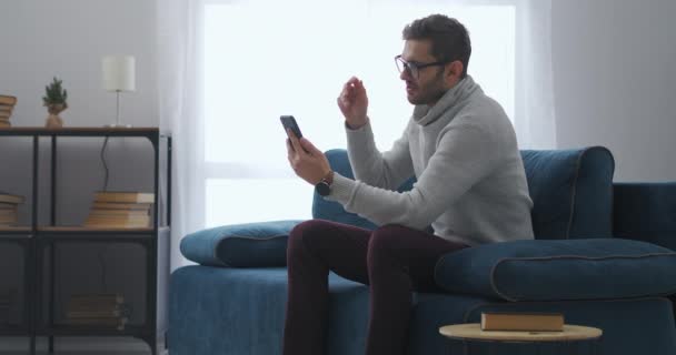 Erwachsener Mann mit Brille streamt in seinem Blog oder sozialen Netzwerken per Smartphone, sitzt zu Hause auf der Couch — Stockvideo