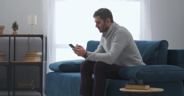 Man is met behulp van smartphone zitten thuis, gokken online in de toepassing en winnen, vreugde emotioneel — Stockvideo