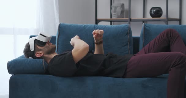 Joven es relajante tumbado en el sofá en fin de semana y el uso de pantalla montada en la cabeza, el control de la pantalla virtual — Vídeo de stock