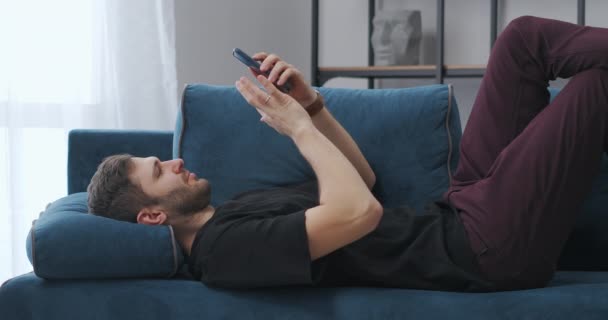 Šťastný chlap leží na gauči a pomocí smartphonu, vyhrávat loterii nebo hru v aplikaci a radovat — Stock video