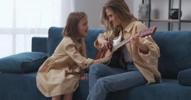 Mutlu anne ve kızı birlikte gitar çalıyor, kız kadını alkışlıyor.