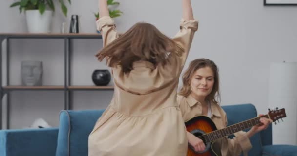 迷人的小女孩在客厅里打转和跳舞，成年女人在弹吉他、玩乐和娱乐 — 图库视频影像