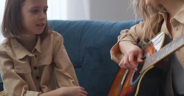 Yetişkin bir kadın küçük kızı için gitarda şarkı çalıyor, kız merakla bakıyor ve annesiyle konuşuyor. — Stok video