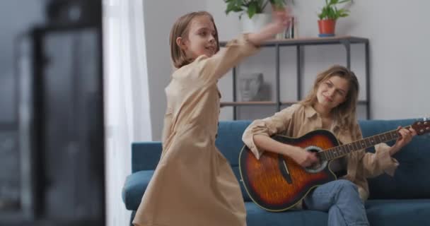 Szczęśliwa kobieta gra na gitarze i patrząc z miłością na jej tańczącej córeczce, matka spędza czas ze swoim dzieckiem — Wideo stockowe