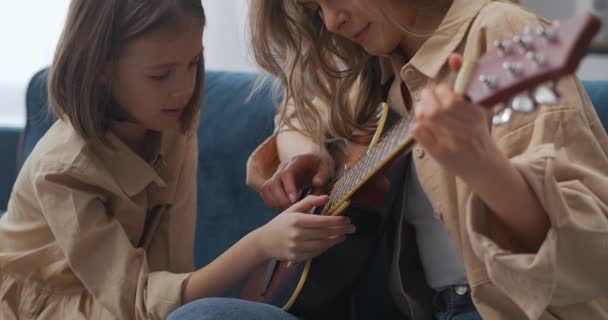 Matka i córka bawią się razem w domu, kobieta gra na gitarze, a ciekawe dziecko dotyka strun — Wideo stockowe