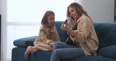 Sarışın kadın gitarda melodi çalıyor ve küçük kızı anne ve çocuğun düetini söylüyor.