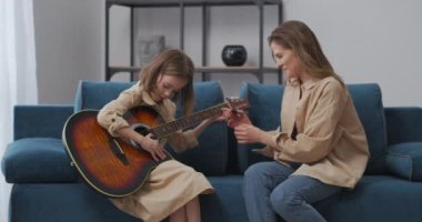 Küçük kız gitar çalmayı öğreniyor, anne ona yardım ediyor ve öğretmenlik yapıyor, aile evde vakit geçiriyor.
