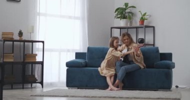 Anne ve kızı evde müzik yapıyorlar, birlikte gitar çalıyorlar oturma odasında kanepede oturuyorlar.