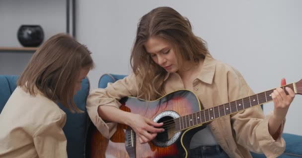 Fin de semana familiar, madre e hija pequeña están tocando la guitarra y cantando canciones, la mujer está enseñando a su hija a tocar la guitarra — Vídeo de stock