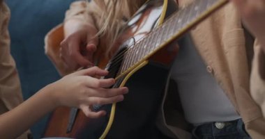 Kadın gitar çalıyor ve meraklı kızı tellere bakıyor ve ona dokunuyor.