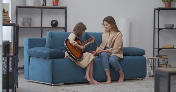 Mujer está enseñando a su hija a tocar la guitarra, lección de música en casa en fin de semana, fin de semana familiar en casa — Vídeo de stock