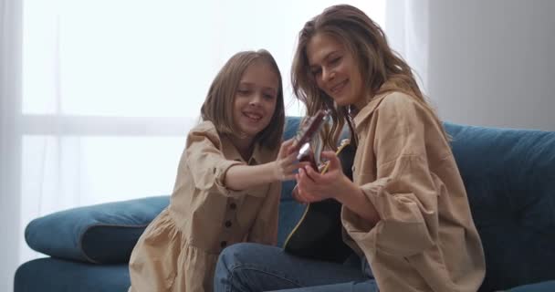 Szczęśliwa matka i córka grają razem na gitarze w weekend w domu, kobieta uczy swoje dziecko grać — Wideo stockowe