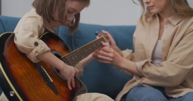 Anne ve kızı gitar çalmayı öğreniyor, kadın çocuğuna yardım ediyor, mutlu aile vakit geçiriyor.