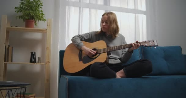 La niña pasa los dedos de su mano derecha sobre las cuerdas varias veces y detiene el sonido de las cuerdas con su palma. Un joven músico está aprendiendo a tocar la guitarra clásica. — Vídeos de Stock