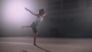 Genç sanatsal jimnastikte yer egzersizleri yapan ergen kız tek ayak üstünde poz veriyor.