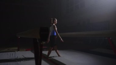 Genç atletik kadın akşam jimnastik salonunda antrenman yapıyor, jimnastikçi kız dengeyi sağlamak için yaklaşıyor.