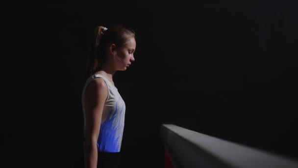 Competition of junior gymnasts, teen girl is standing near balance beam, preparing to start of performance, portrait shot in sports hall — Stock Video
