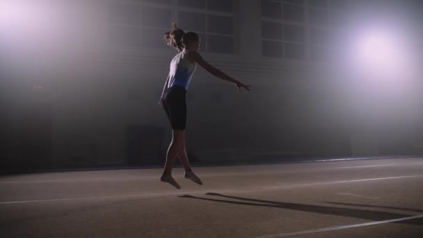 Jonge sportvrouw traint in gymnastiek hal, het uitvoeren van vloeroefening, springen over de lente verdieping, sportieve vrouwelijke silhouet — Stockvideo