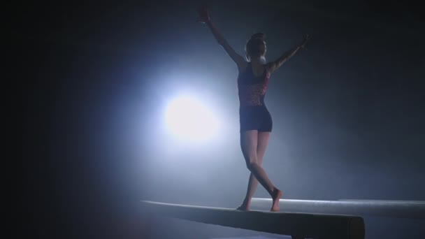 Joven gimnasta femenina está realizando en la viga de equilibrio en la sala de gimnasio oscuro, deporte y actividad para los jóvenes — Vídeos de Stock