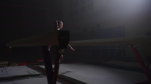 Adolescente chica gimnasta está entrenando en sala de gimnasia por la noche, chica deportiva se acerca a equilibrio viga — Vídeos de Stock