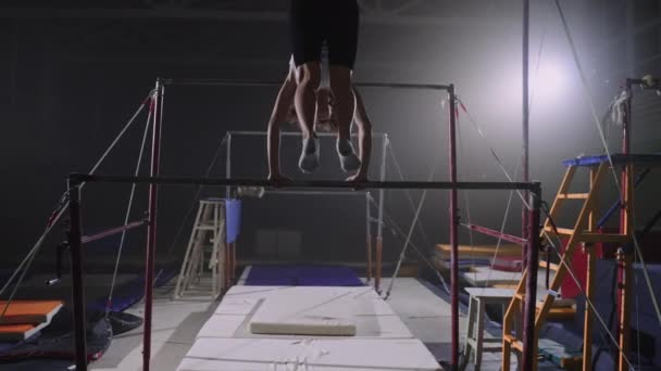 Jong sportief meisje is training op ongelijke bars in sporthal, vrouwelijke artistieke gymnastiek, slow motion schot, achteraanzicht — Stockvideo