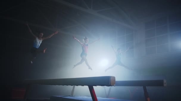 Entrenamiento de las niñas gimnastas en la viga de equilibrio, tres adolescentes se mueven de forma síncrona en el pabellón deportivo — Vídeo de stock