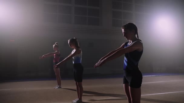 Trening młodych gimnastyczek, trzy sportowe nastolatki wykonują salta do tyłu w hali sportowej — Wideo stockowe