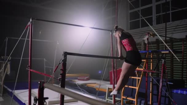 Sportig kvinnlig gymnast utför övningar på ojämna barer i gymnastiksalen på kvällen, kvinnlig konstnärlig gymnastik — Stockvideo