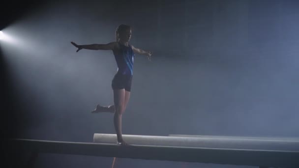 Niña deportiva está realizando en el haz de equilibrio solo en la sala de deportes oscuros, deportista principiante, tiro en cámara lenta — Vídeos de Stock