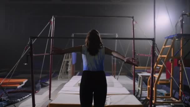 Молодая спортсменка выступает на неровных барах в гимнастическом зале, женских соревнованиях по художественной гимнастике — стоковое видео