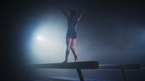 Молодая спортсменка на соревнованиях по художественной гимнастике, женщина-гимнастка выступает на бревне баланса, вид сзади — стоковое видео