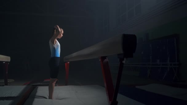 활동적 인 십 대 소녀는 어두운 체조 홀에서 균형 줄기를 사용하여 미술 체조를 훈련시키고 있다 — 비디오