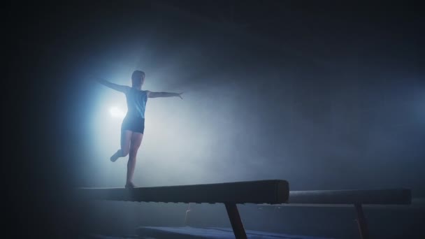 스포츠 학교에서 어린이 예술 체조 시합을 하고 있는 십 대 소녀는 균형 광선인 실루엣으로 균형을 잡고 있다 — 비디오