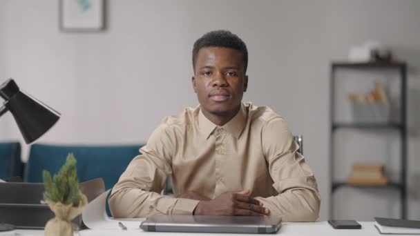 Portré komoly és kedves fiatal fekete férfi ül az asztalnál az otthoni irodájában, afro-amerikai srác — Stock videók