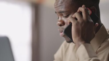 Afro-Amerikalı iş adamı cep telefonuyla konuşuyor. Ev ya da iş yerinden. Genç siyahi adamın yüzüne yakından bakıyor.